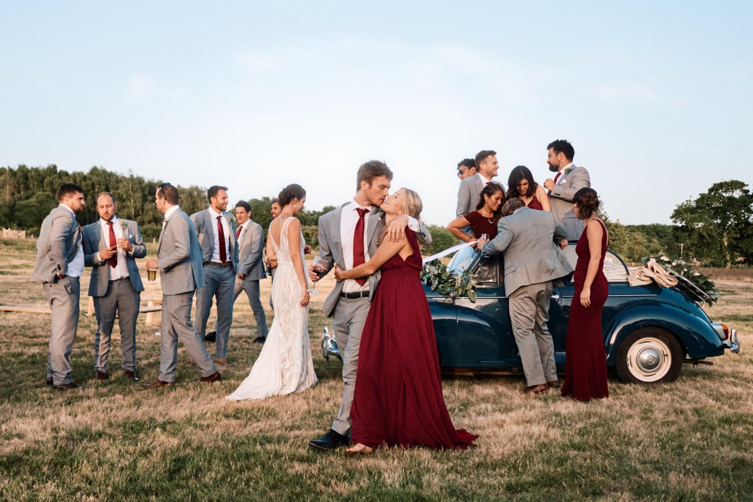 Bridal party climb out of convertible car in a field