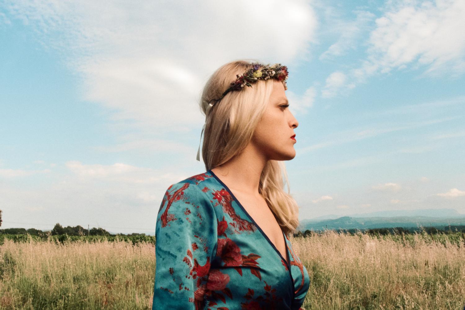 A bridesmaid with floral head piece looks pensively in a field in France