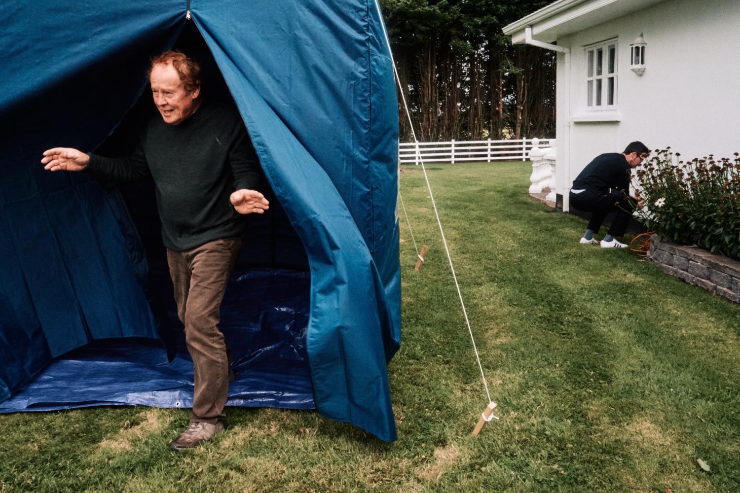 A man exits a blue tent in a garden