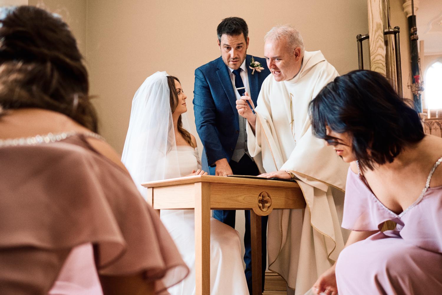 Bride and groom sign marriage certificate in the company of a priest