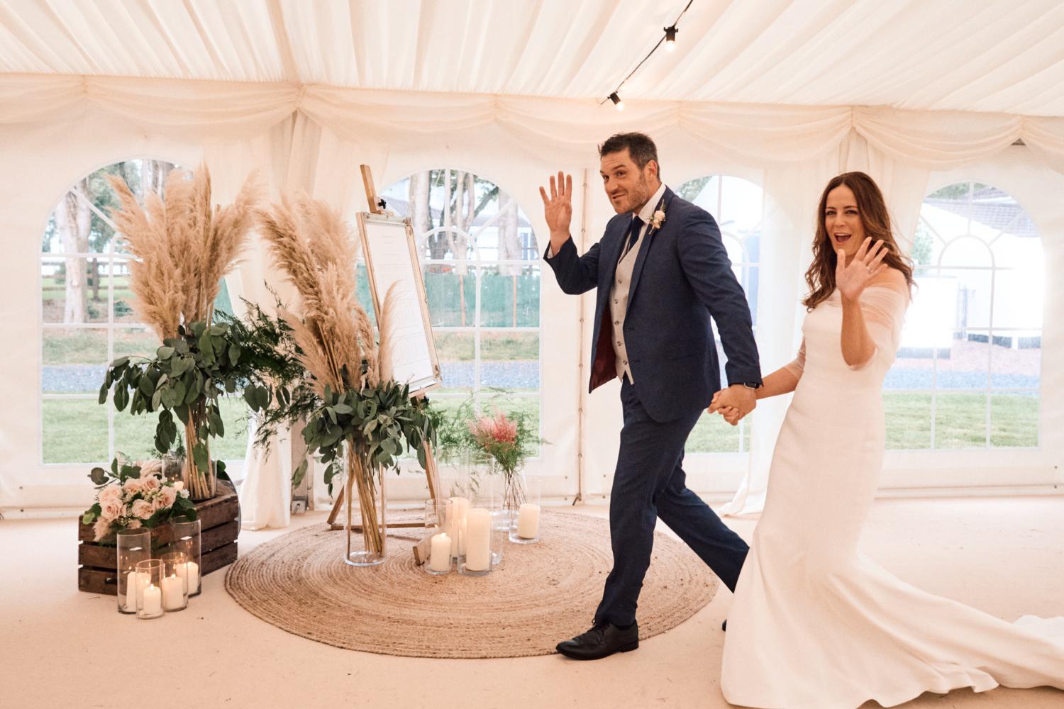 A married couple wave as they enter a marquee wedding reception