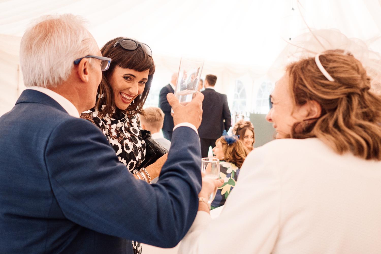 Wedding guests laugh and enjoy drinks in a marquee