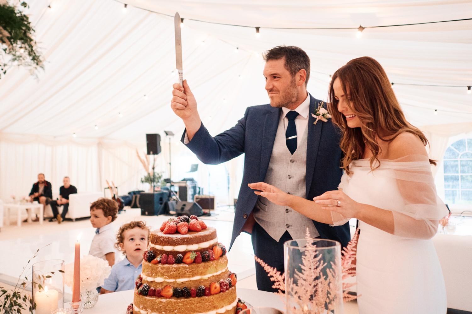 A bride and groom cut their wedding cake in front of a child