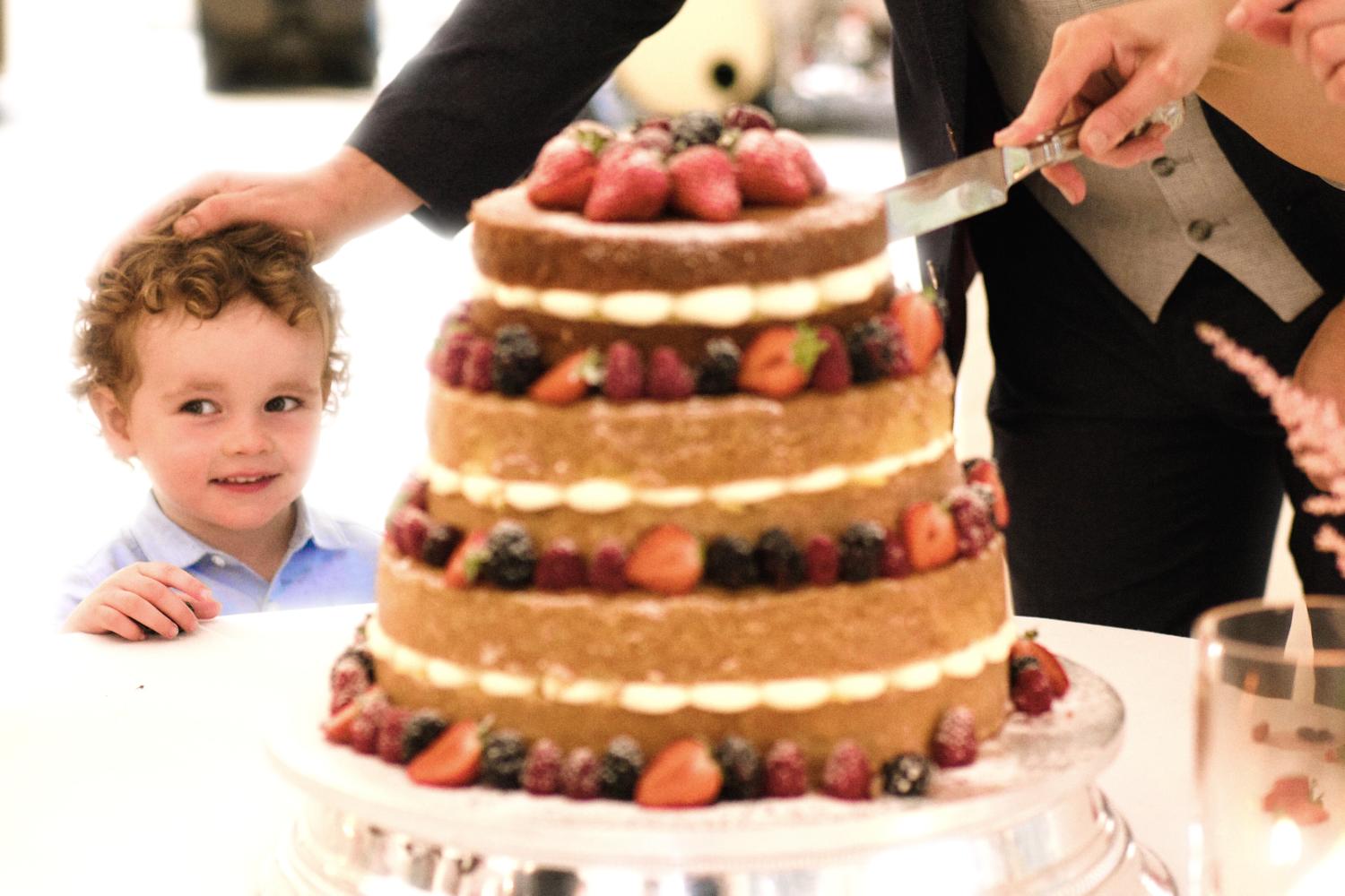 A smiling child is patted on the head by a groom in marquee in front of a wedding cake