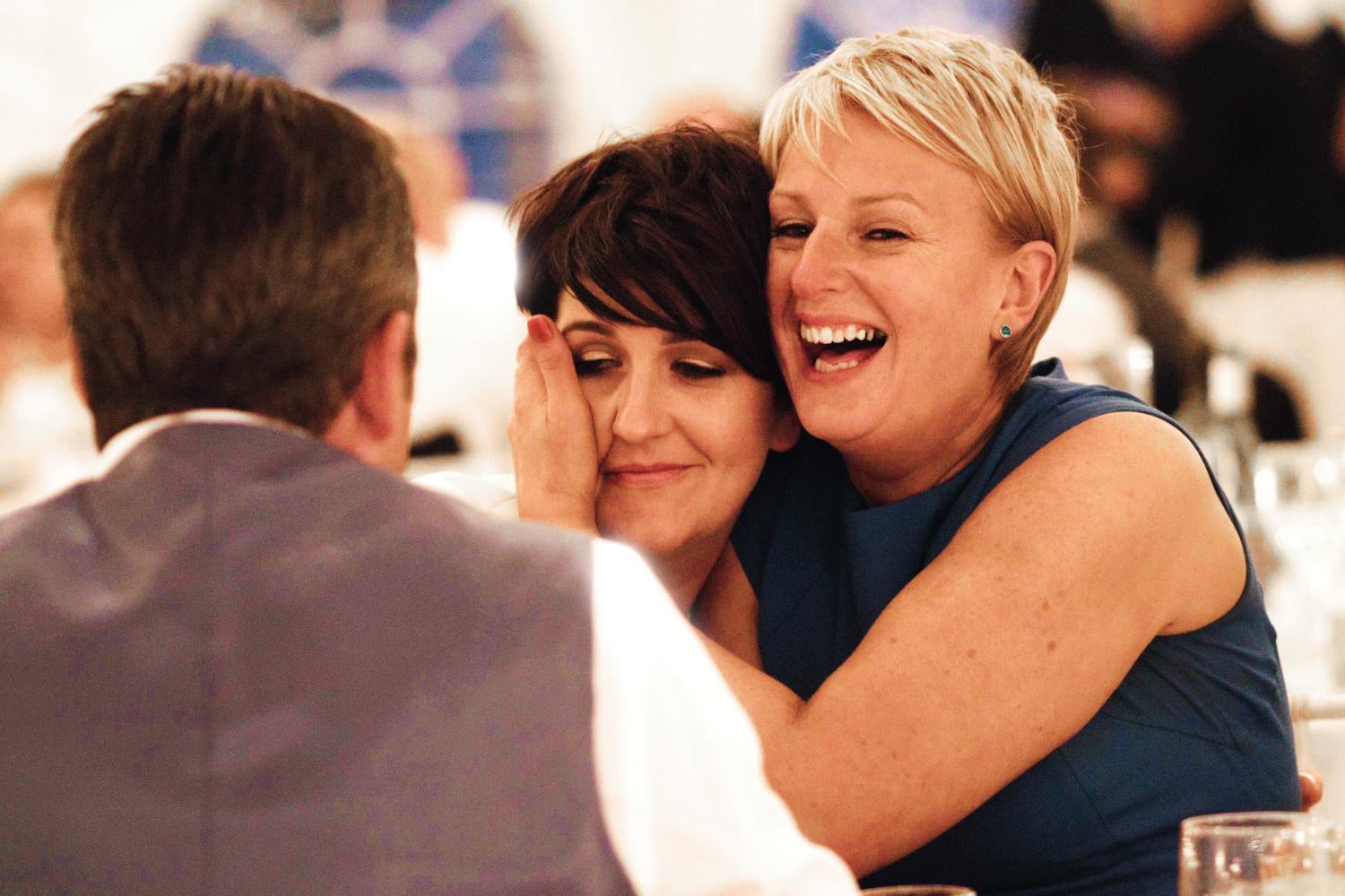 Two women hug and laugh at a wedding