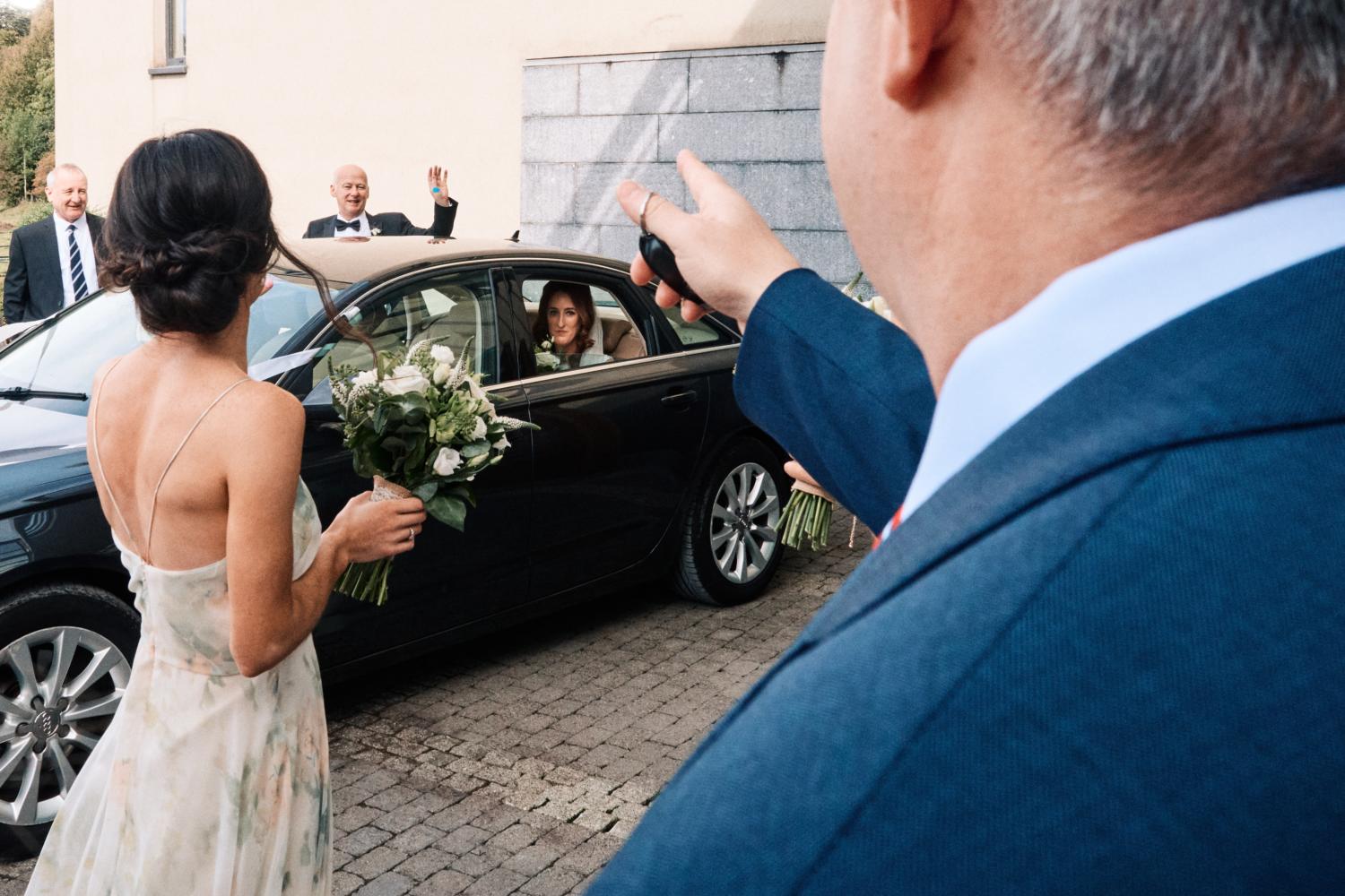A bride and father leave for a wedding in a black car