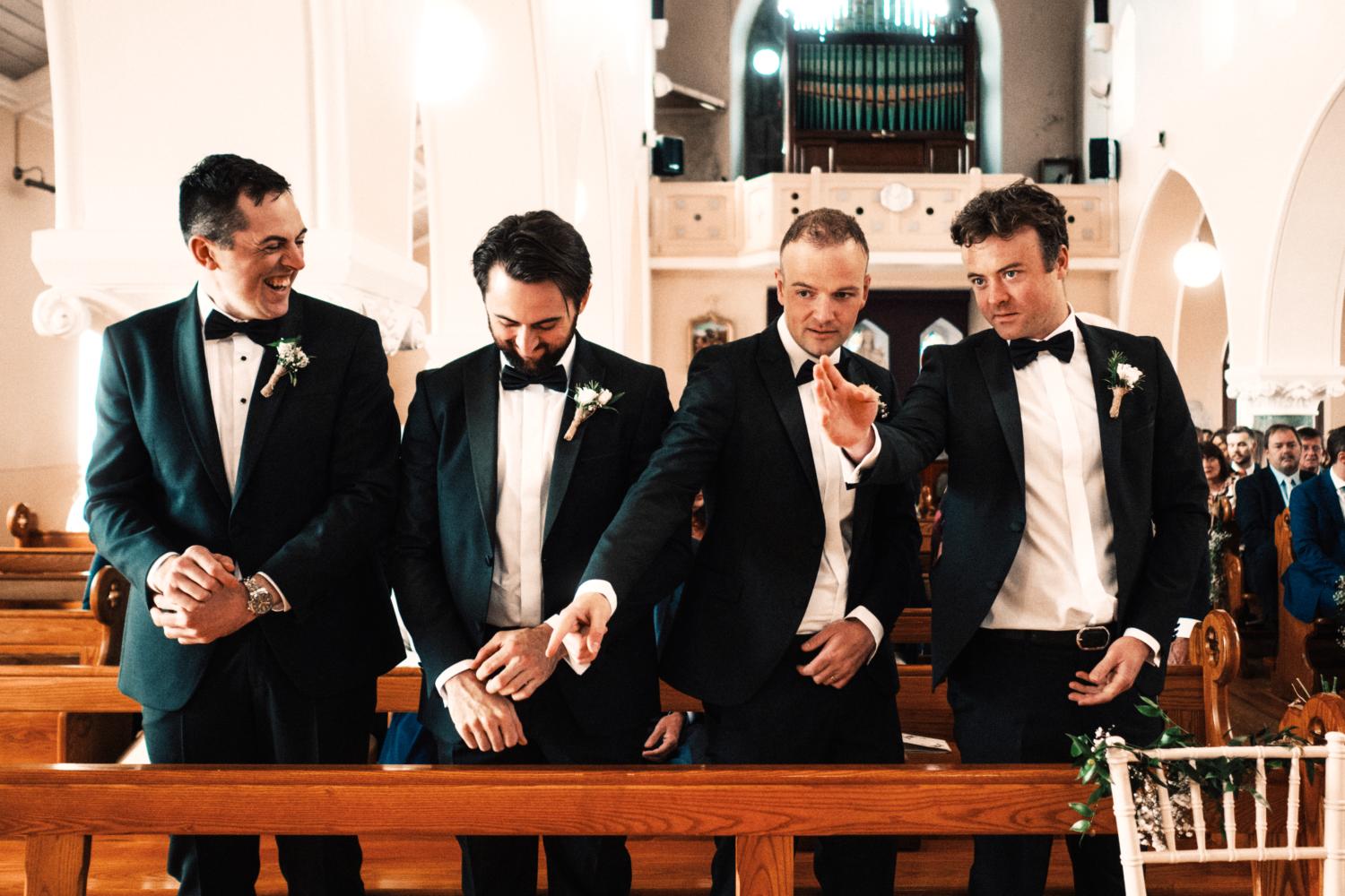 A groom and groomsmen wear tuxedos in a Catholic chapel