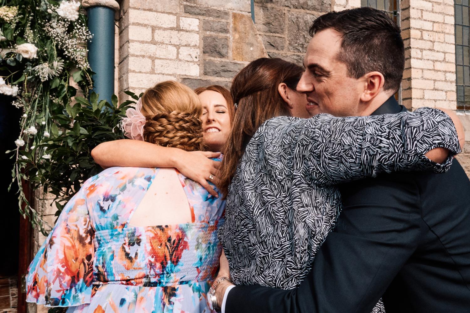 Bride and groom hug friends outside a chapel