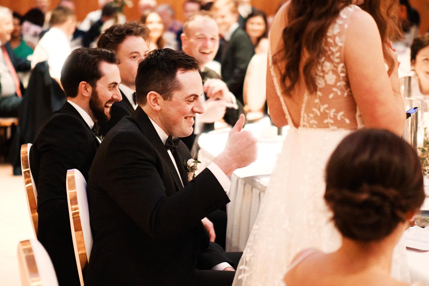 A groom raises his thumb in an approving manner during the bride's speech