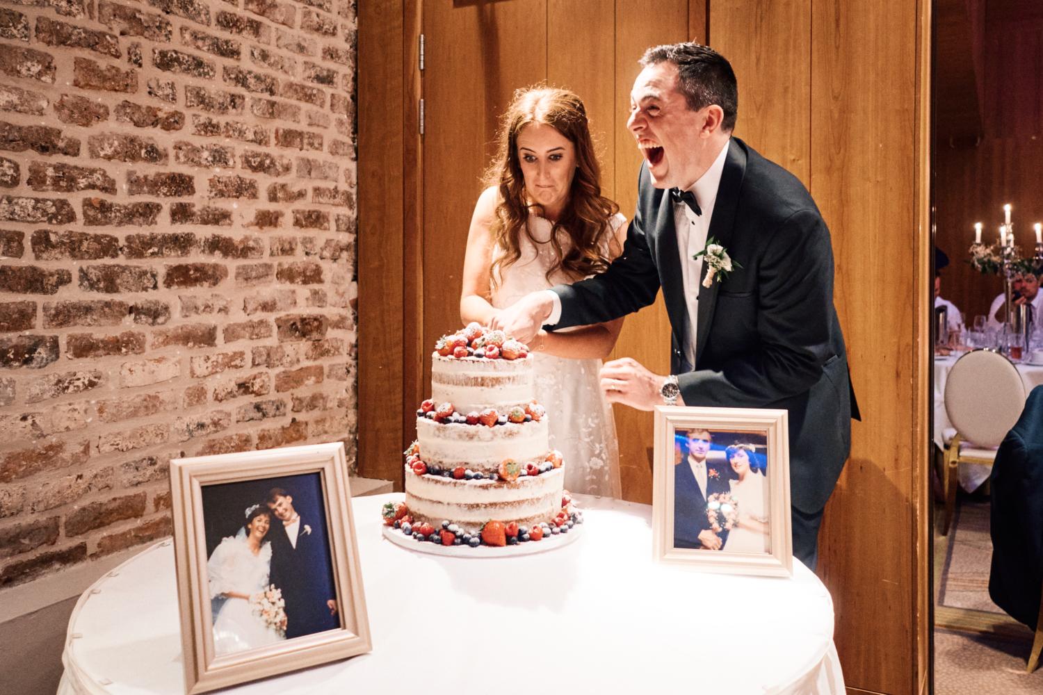 A bride and groom laugh while cutting the cake