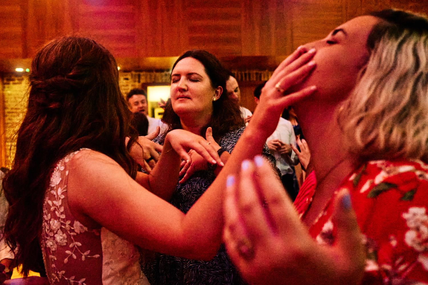 A bride touches her friend's face on a dance floor