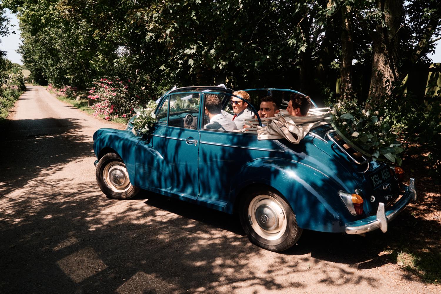 Groom and friends drive away in a blue convertible vintage car