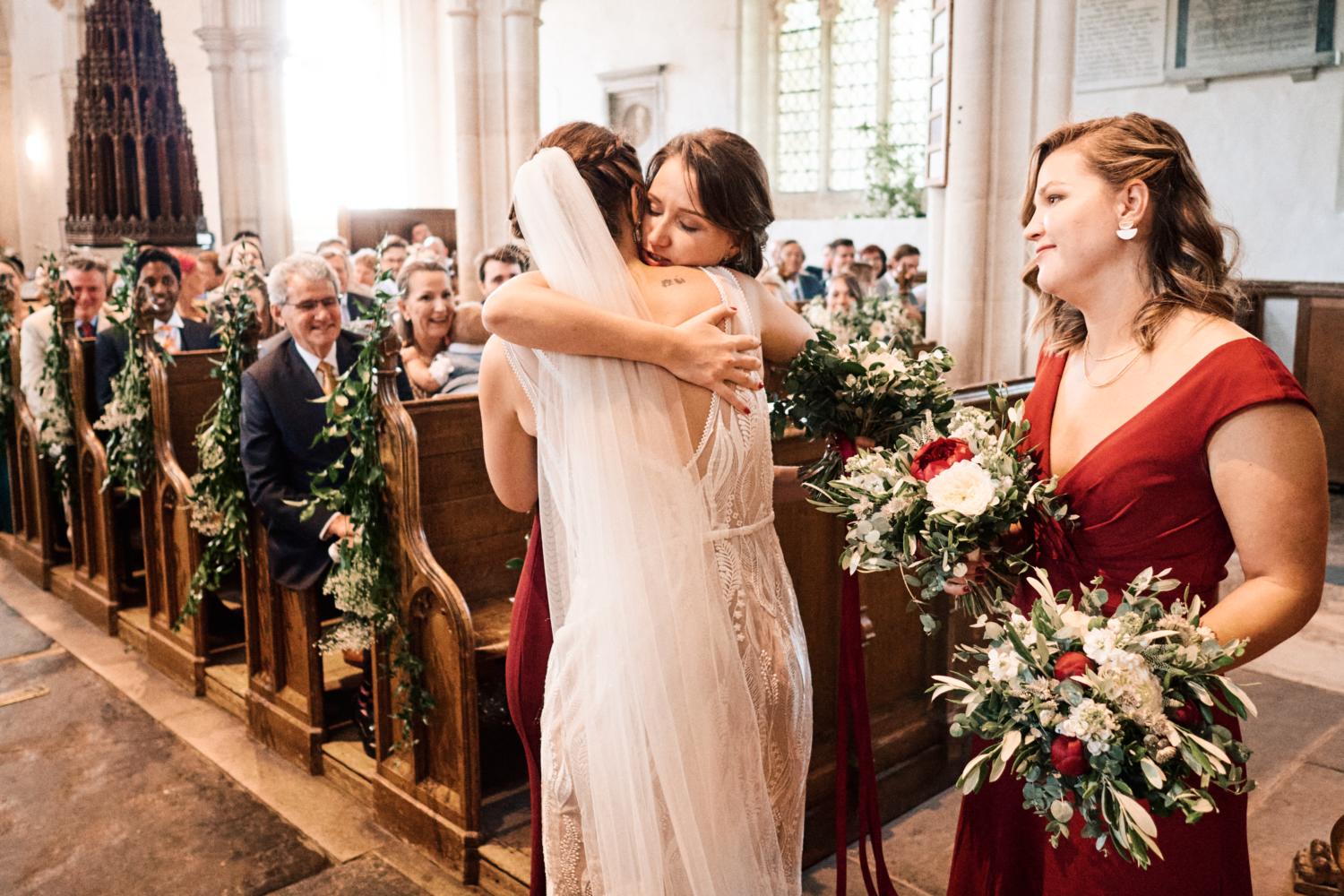 A bride affectionarely hugs her sister during a wedding ceremony in Ewelme, England