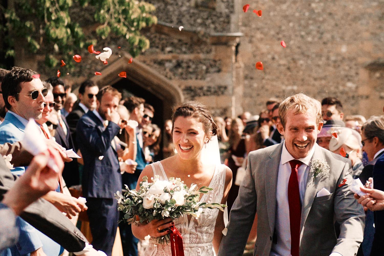 Guests throw confetti at bride and groom outside Ewelme Church