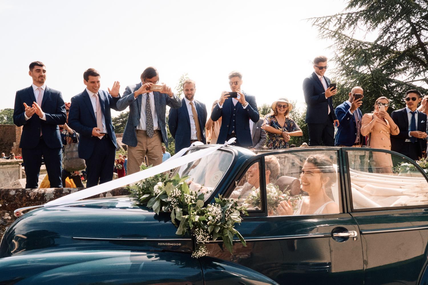 Bride and groom drive away from church in a blue convertible car