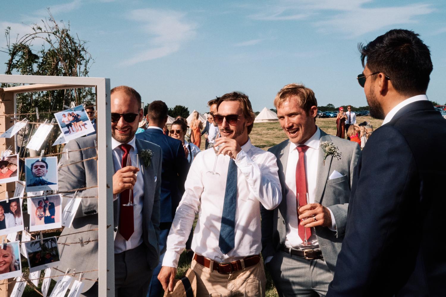 Groomsmen laugh and enjoy drinks at an outdoor wedding reception