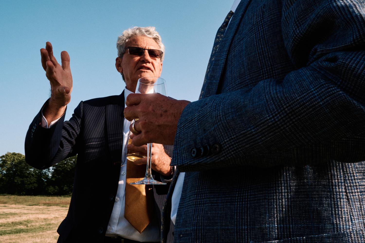 A man in sunglasses gestures to a friend with his hand