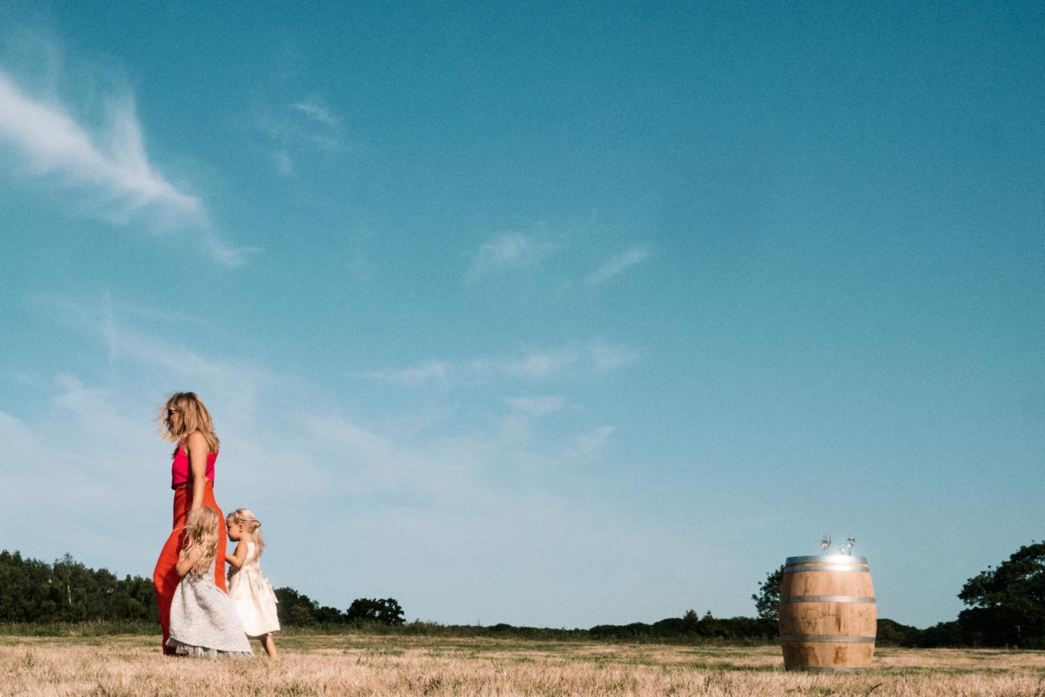 A mother walks her daughters in the opposite direction of a barrel in a field