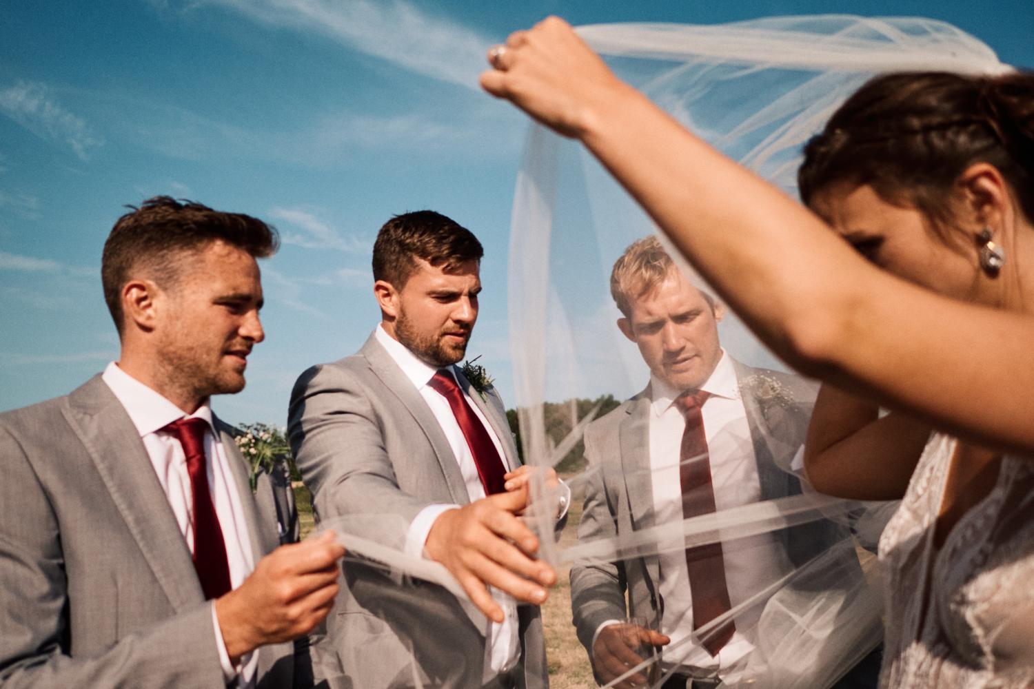 Groomsmen help the bride with her veil