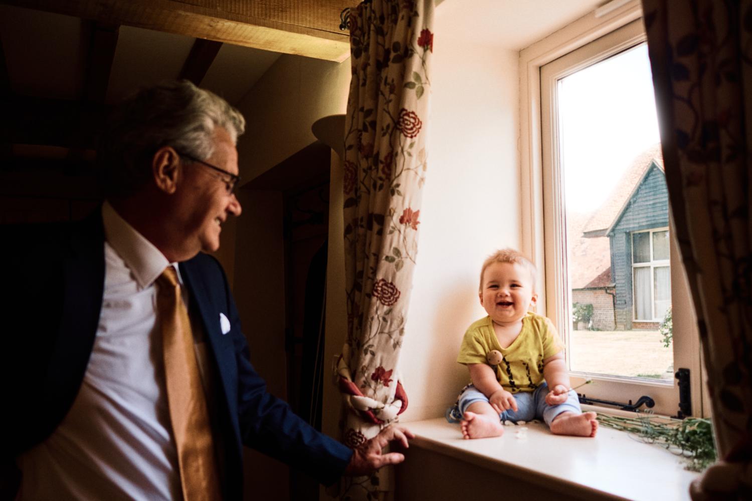 A laughing baby sits in a window frame