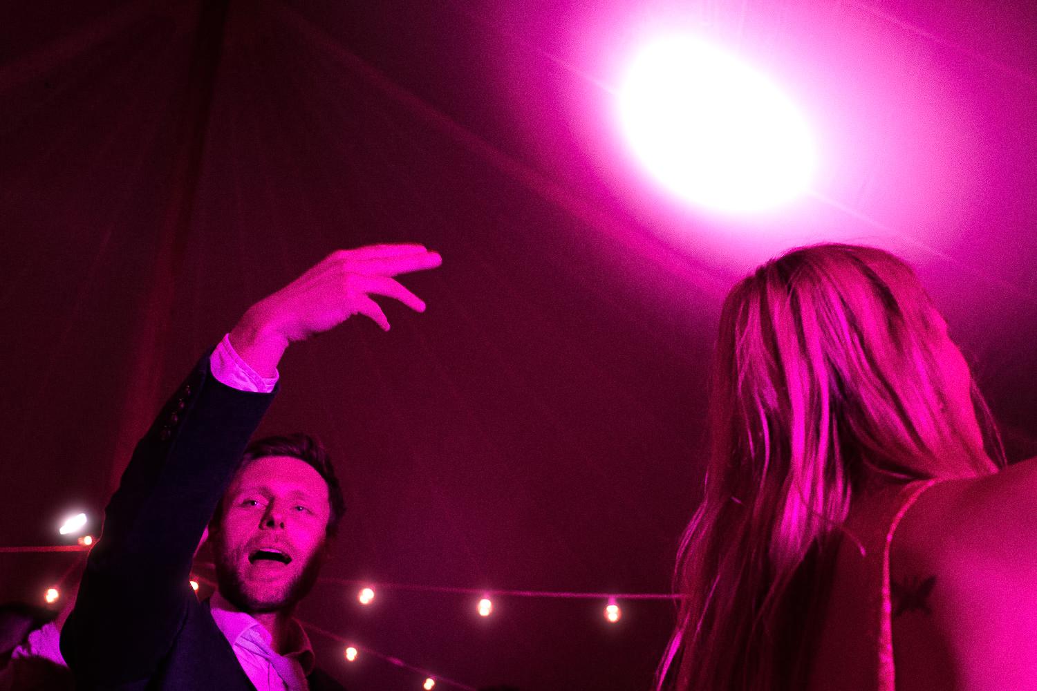A wedding guest raises his hand on the dancefloor, in purple light