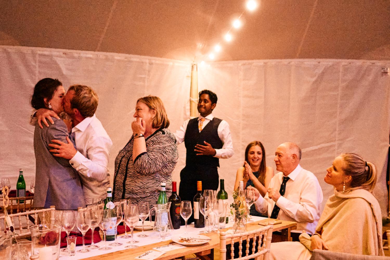 Bride and groom kiss in front of their friends in a marquee