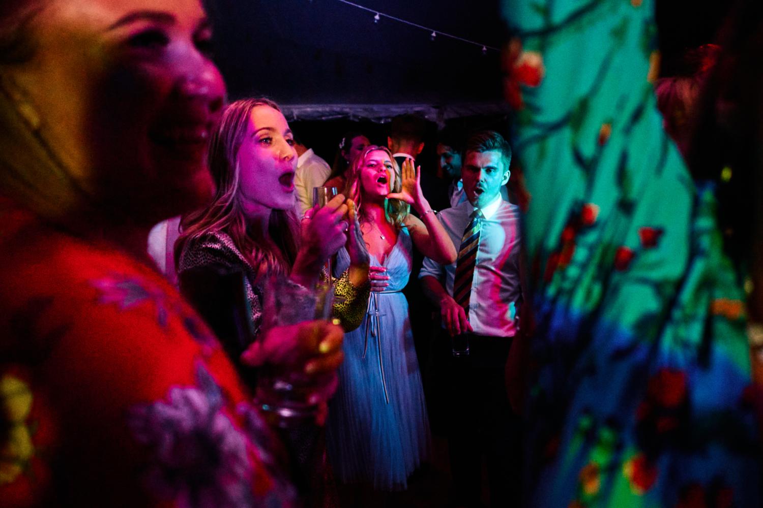 Colourful lights illuminate singing dancers at a marquee wedding reception